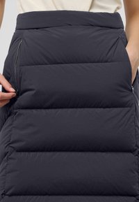Jupe matelassée en gris foncé, avec un design en sections verticales et des poches zippées de chaque côté pour plus de fonctionnalité.
