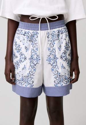 Short blanc avec imprimé floral géométrique bleu et taille et ourlet rayés bleus, noué à l'avant avec un cordon blanc.