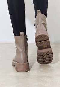 Botas de tobillo de cuero marrón con cremalleras laterales, parte superior texturizada y suelas de goma con un patrón de relieve para mayor tracción.