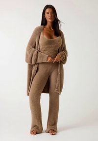 Tan, fuzzy loungewear set featuring a sleeveless top and wide-leg pants, layered with a button-front cardigan; soft texture and relaxed fit.