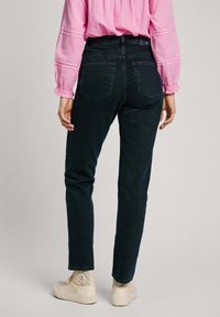 Jeans de mezclilla oscura con corte recto, que cuentan con dos bolsillos traseros y una cinturilla de altura media, combinados con zapatillas altas blancas.