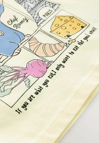 Lys gul bomulds t-shirt med et cartoon-agtigt musse-kok, madvarer og tekst. Inkluderer billeder af ost, grøntsager og et croissant.