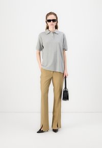 Grå poloshirt med korte ærmer, lysebrune skræddersyede bukser med sideslids og en sort håndtaske. Modellen bærer sorte solbriller og høje sko.