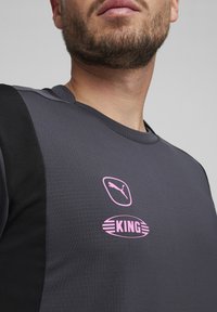 Hallitus hallen spordisärk mustade aktsentidega, millel on roosa Puma logo ja "KING" graafika rinnal. Tekstureeritud kangas, ümmargune kaelus.