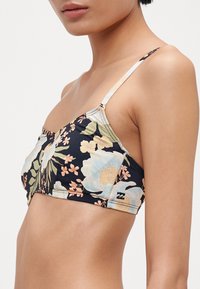 Blomstrete bikinitopp med svart base, lyseblå og ferskenfargede blomster, justerbare stropper og en liten logo detalj på siden.