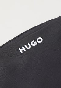 Gros plan d’un tissu noir avec un texte blanc en relief indiquant "HUGO" sur le bord supérieur du matériau.