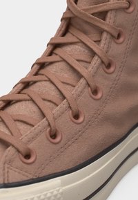 Κοντινό πλάνο ροζ σκόπιμης σουέντ ψηλής μπότας με κορδόνια και οπές στο ίδιο χρώμα, λευκή καουτσούκ σόλα και μαύρη λεπτομέρεια περιγράμματος.