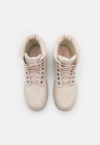 Botas de tobillo beige de FILA con cuellos acolchados, cordones acentuados en rosa y suelas robustas vistas desde arriba sobre un fondo blanco.