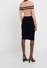 Geripptes Strickoberteil mit langen Ärmeln in Blush mit schwarzen Streifen, kombiniert mit einem schwarzen, knielangen Bleistiftrock. High Heels runden den Look ab.