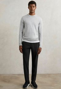 Lichtgrijze langemouwentrui, zwarte taperingbroek en zwarte sneakers met witte zolen. De trui heeft een ronde hals en een slim fit.