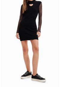 Robe noire côtelée avec manches longues transparentes et encolure en forme de cœur. Associée à des baskets noires à semelles en caoutchouc.