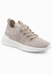 Scarpa sportiva beige chiaro con tomaia a maglia, lacci elastici, colletto imbottito e suola bianca testurizzata con un motivo a onde.