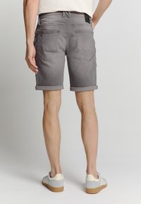 Grijze denim shorts met opgerolde boorden, met twee achterzakken en een zwart etiket bij de tailleband. Draag ze met lichtgrijze sneakers.