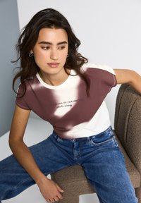 Kortærmet, afslappet T-shirt i cremefarvet og maroon med et gradientdesign, der har teksten "Audition of Confidence" i sort.