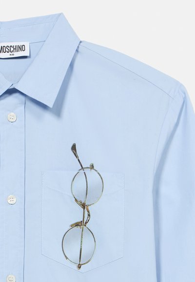 Ανοιχτό μπλε πουκάμισο με κουμπιά και τσέπη. Στρογγυλά, διάφανα γυαλιά με χρυσούς σκελετούς τοποθετημένα στην τσέπη, μ ε διακριτική γυαλάδα.