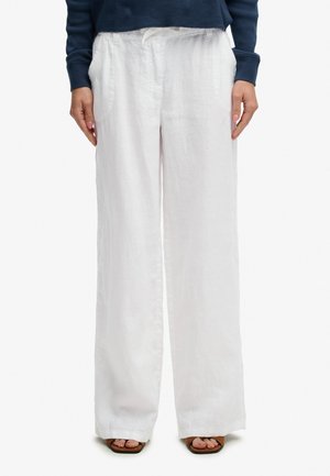 Osoba nosząca luźne białe lniane spodnie z kieszeniami, w połączeniu z granatową bluzką z długim rękawem i sandałami z odkrytymi palcami.