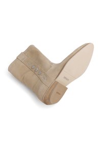 Bottine en suédine beige avec un petit talon bloc. Comprend un matériel circulaire décoratif sur le côté et une semelle en caoutchouc texturée.