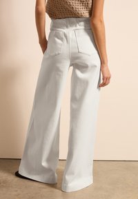 Pantalones de pierna ancha en tejido gris claro, con una cintura alta, bolsillo trasero y un acabado texturizado. Adecuados para uso casual.
