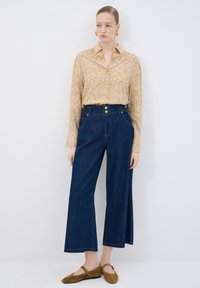 Camisa de botones de manga larga, color beige claro, con un patrón floral, combinada con jeans de tiro alto de pierna ancha en oscuro azul y bailarinas marrones.