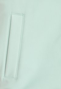 Light mint green fabric with a smooth texture features a rectangular patch detail, stitched edges, and a matte finish.