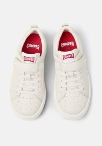 Sneaker bianche in pelle con una texture liscia, dotate di una fascia in Velcro, design classico con lacci e dettagli rossi sulla soletta interna e sull'etichetta del marchio.
