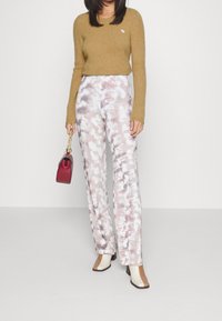 Maglione marrone lavorato a maglia, pantaloni a gamba larga a fantasia pastello e stivaletti con tacco bicolore. Piccolo logo sul maglione e una borsa bordeaux.