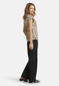 Short-sleeve top with a black leaf pattern on a cream background, paired with loose black pants and strappy black sandals.