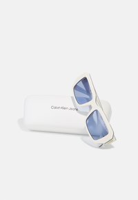 Sončna očala Calvin Klein Jeans z belim okvirjem in svetlo modrimi lečami, z geometrijskim dizajnom in minimalnim blagovnim znamkom na etui.
