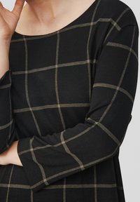 Czarny, długi rękaw bluzka z wzorem w kratkę z jasnobrązowymi liniami. Materiał wydaje się miękki, ma luźny krój i szeroki dekolt.