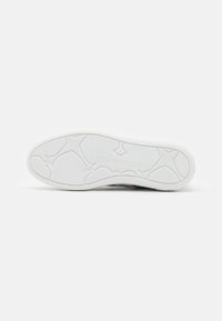 Suela de zapatilla deportiva con un material de goma blanca texturizada, con un patrón geométrico y el nombre de la marca en relieve.
