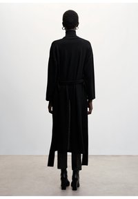 Sort lang cardigan med høj krave, åbent front og bælte til at binde i taljen. Blødt strikmateriale, lige snit og let gennemsigtig ryg.