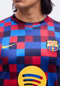 Άτομο που φοράει κονκάρδα FC Barcelona με κόκκινο και μπλε καρό, με ορατά τα λογότυπα της Nike και της Spotify στο στήθος.