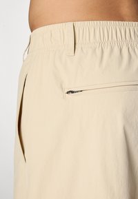 Beige shorts med elastisk liv, med en sidelomme med glidelås og glatt, lett stofftekstur. Designet med minimale sømmer.