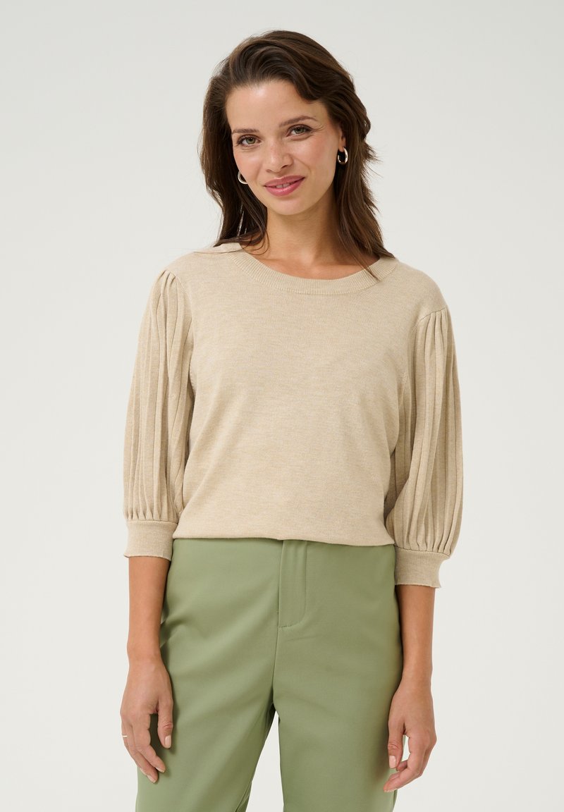 Beige knit pullover with ribbed puff sleeves, round neckline, and lightweight texture. Paired with green high-waisted pants.
