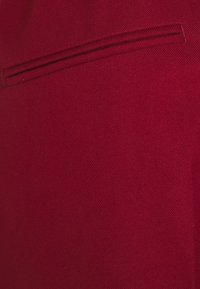 Tissu rouge avec une texture lisse ; présente un motif de tissage diagonal subtil et une couture décorative en passepoil sur le bord supérieur.