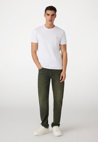 Hvid bomulds T-shirt med et lille rødt trekantlogo, parret med grønne denimjeans og hvide sneakers, der har en afslappet pasform og lige snit.