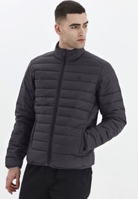Svart vadderad jacka med hög krage och dragkedjestängning, som har horisontellt quiltade sektioner och en lätt design.