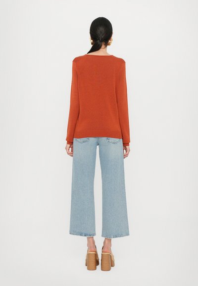 Rust-colored knit sweater with a round neckline, paired with wide-leg light blue jeans and tan platform heels.