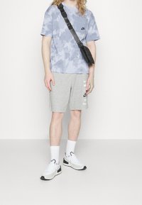 Nike blue patterned t-shirt, gray shorts with logo, white socks, and white sneakers. Features a black crossbody bag and straight fit.