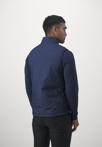 Gilet blu navy con colletto alto, texture liscia e design aerodinamico, caratterizzato da una vestibilità aderente e dettagli di cucitura a contrasto.