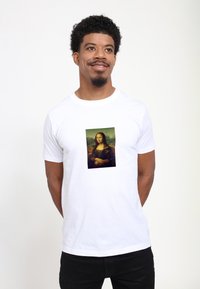 Hvid bomulds t-shirt med et trykt billede af Mona Lisa i en rektangulær ramme på forsiden. Korte ærmer, rund halsudskæring.