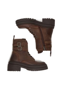 Hnedé kožené členkové topánky s hrubou podrážkou, vázaním na šnúrky vpredu, bočným zipsom a dvojitými prackami. Vyznačujú sa robustnou textúrou a protišmykovým gripom.