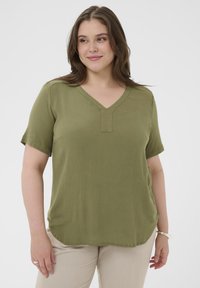 Haut à manches courtes vert olive avec un col en V et un tissu texturé, présentant un détail subtil sur le panneau avant et un ourlet arrondi.