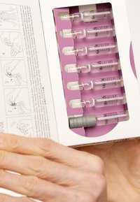 Ampoules en plastique transparent dans un emballage blanc et violet, contenant un capuchon ergonomique gris. Instructions imprimées à l'intérieur de la boîte.