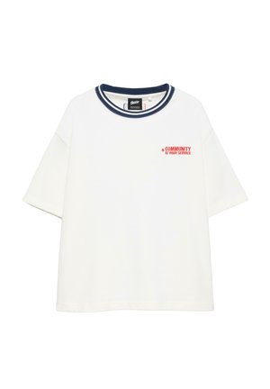 T-shirt blanc manches courtes avec col rayé bleu marine et texte rouge "COMMUNITY AT YOUR SERVICE" sur le côté gauche de la poitrine.