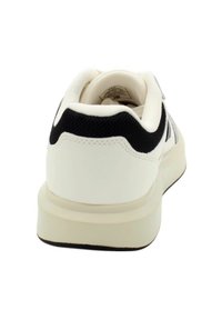 Sneaker bianco con un contrafforte nero testurizzato, una parte superiore liscia e una suola spessa color crema. Presenta un design minimalista e senza motivi visibili.