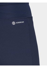 Tamsiai mėlyna AEROREADY sportinė medžiaga, pasižyminti lygiu paviršiumi ir maža balta logotipo detalė šone, su prigludusia forma ir elastingu dizainu.