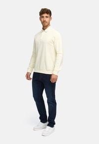 Lys gul genser med krage og lange ermer, kombinert med mørkeblå jeans og hvite joggesko. Mykt stoff, avslappet passform.