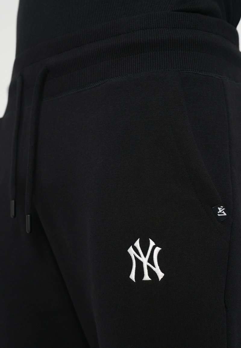 Black sweatpants with a ribbed waistband, featuring a white embroidered logo on the thigh and side pockets. Soft texture, elastic drawstring.
