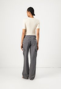 Gray cargo pants with a loose fit, featuring side pockets and a woven texture. Paired with a fitted cream short-sleeve top.